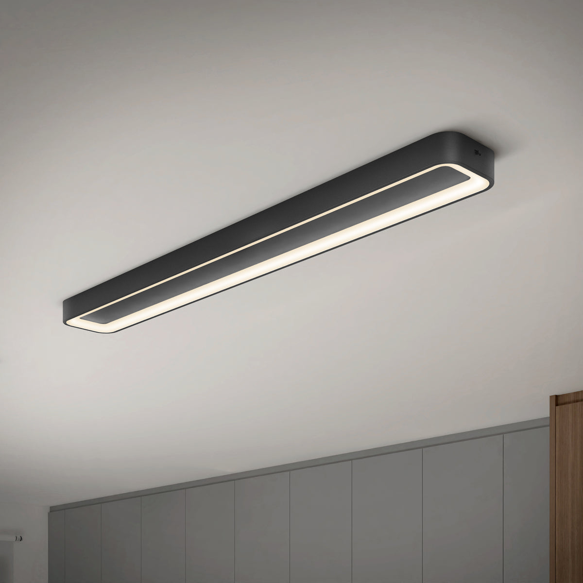 The Artika Aiden 48 in. LED modern flush mount light with a black frame is installed on a white ceiling above gray cabinets, offering customizable 5 CCT lighting.