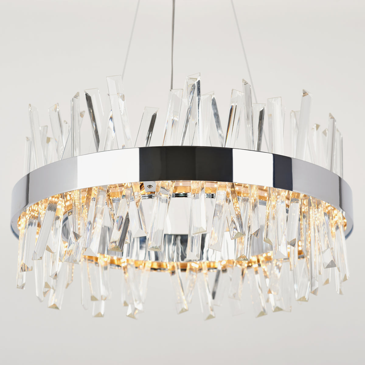The Artika Enchanted LED pendant light features a modern circular design with a chrome frame and jagged crystal accents, suspended by thin wires and glowing warmly against a plain background.