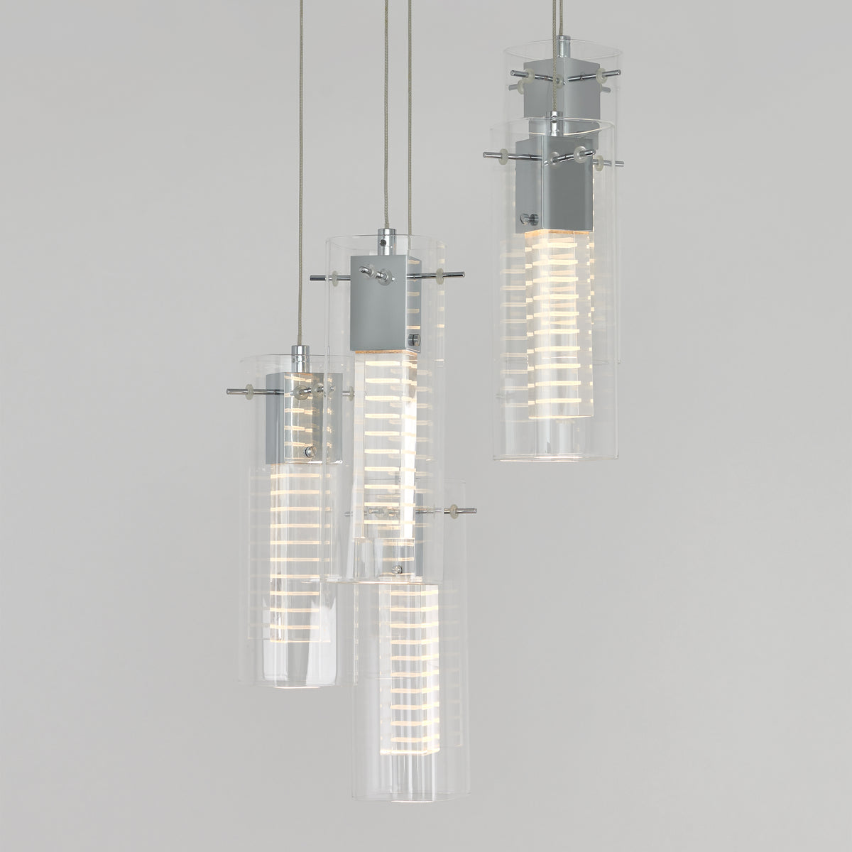 The Artika Hologram 5-light LED pendant features cylindrical glass shades with metallic accents and spiral LED bulbs, suspended at varying heights against a plain light gray background.