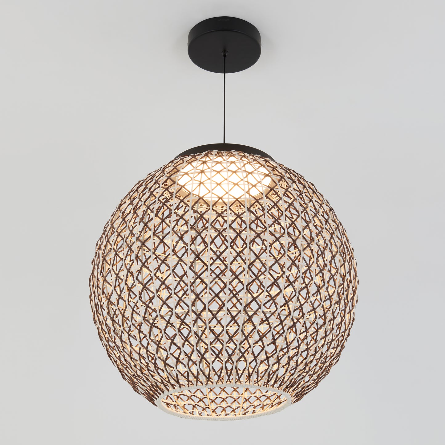 The Artika Benson LED pendant light 5 CCT features a spherical design with a woven brown rattan shade, hanging from the ceiling to emit a warm glow and cast intricate patterned shadows.