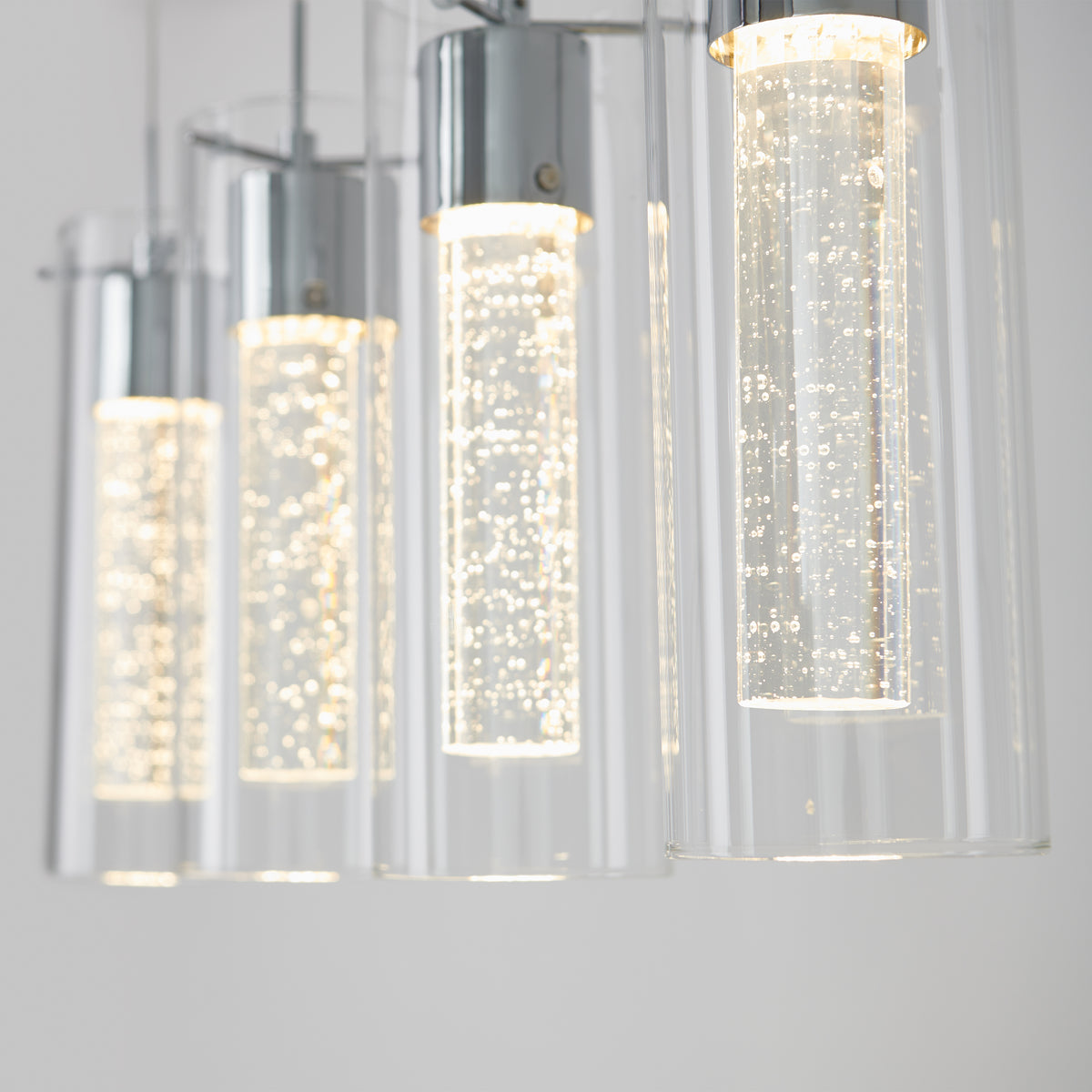 Close-up of Artikas Essence 4-light LED pendant, showcasing cylindrical glass covers with illuminated bubbles inside for a bright, elegant look against a neutral background.