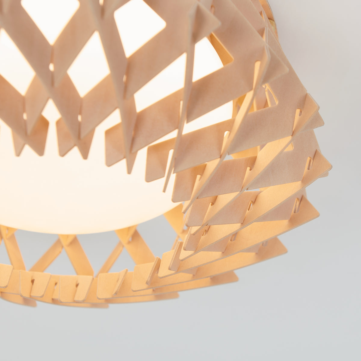 Close-up of the Artika Kiran 13 in. modern LED flush mount light (5 CCT), featuring a geometric wooden lattice design around a frosted globe that forms triangular patterns and emits soft, warm light.