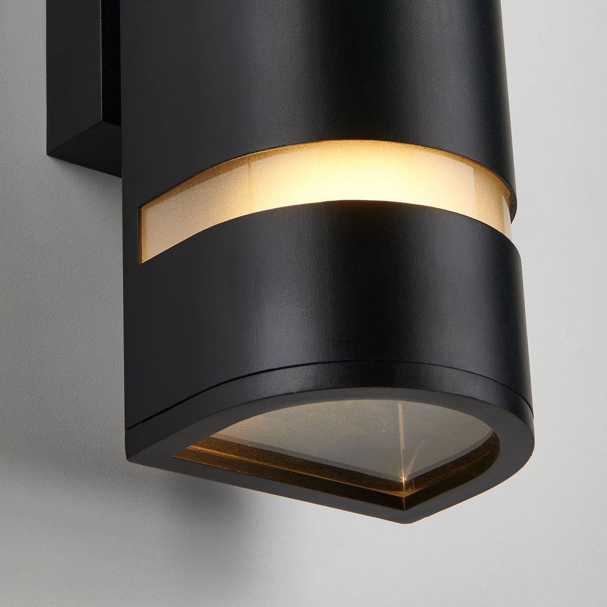 A close-up of the Artika D4 indoor-outdoor wall light, a modern black cylindrical sconce with a horizontal frosted strip near the top that glows warmly, shown mounted on a light-colored wall.