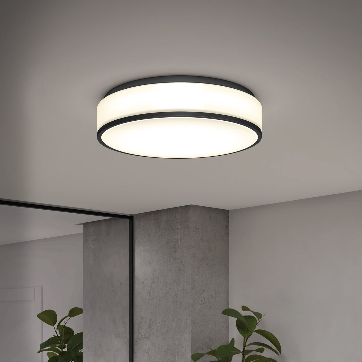 The Artika Giada 15 in. LED modern flush mount light with black trim is installed on a white ceiling in a minimalist room featuring a gray concrete pillar, large mirror, and green potted plants.