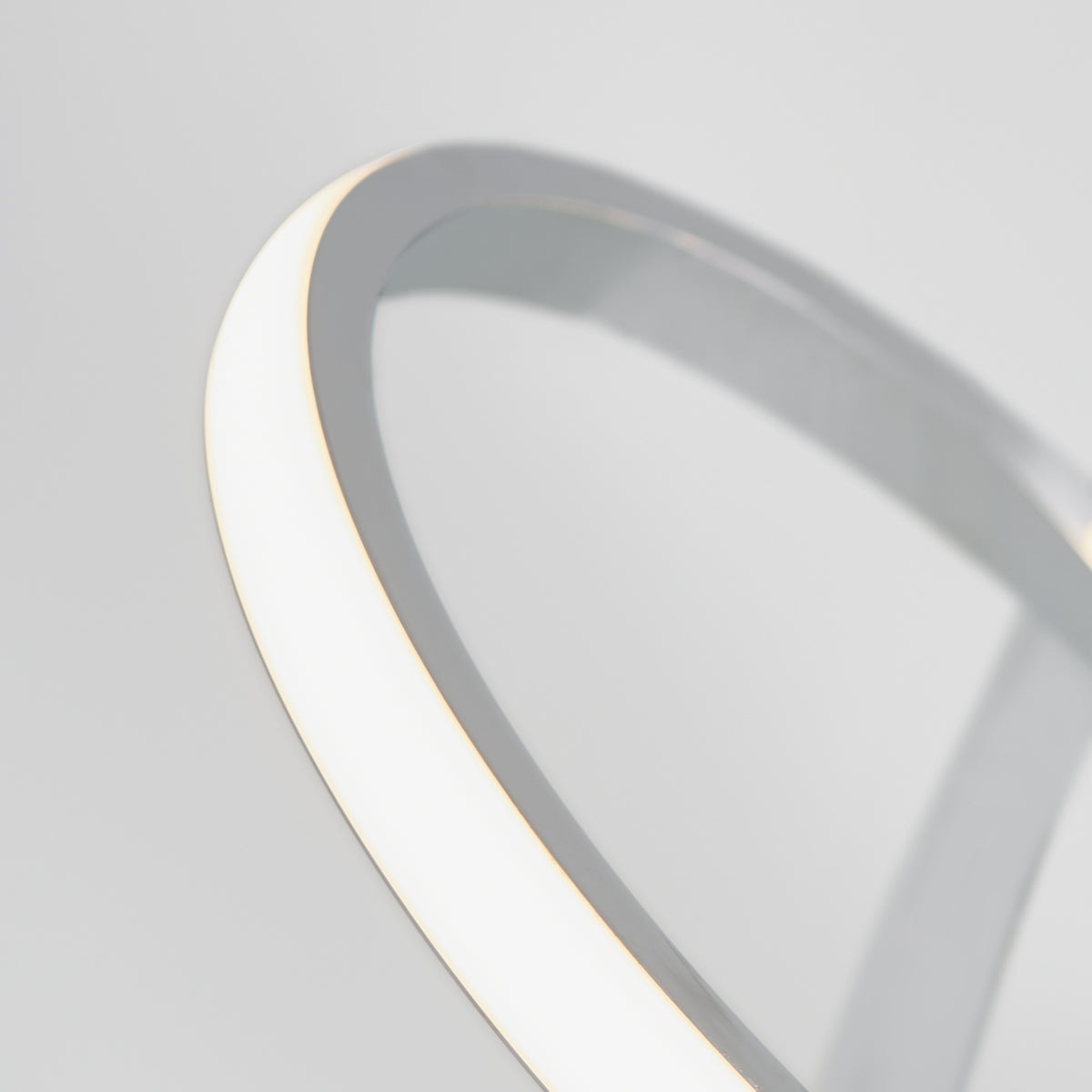 A close-up of the Artika Swirl LED pendant light shows its smooth metallic frame and curved illuminated white strip, capturing the fixtures modern, minimalist design against a plain gray background.