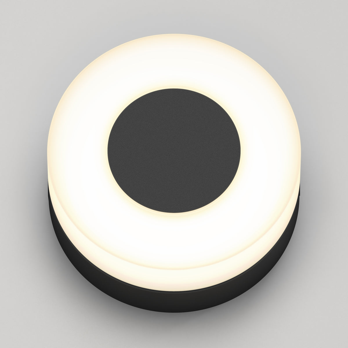 The Ludwig modern LED indoor-outdoor wall light by Artika features a minimalist round design with a black center and glowing white ring, suitable for walls or ceilings, shown against a plain light grey background.
