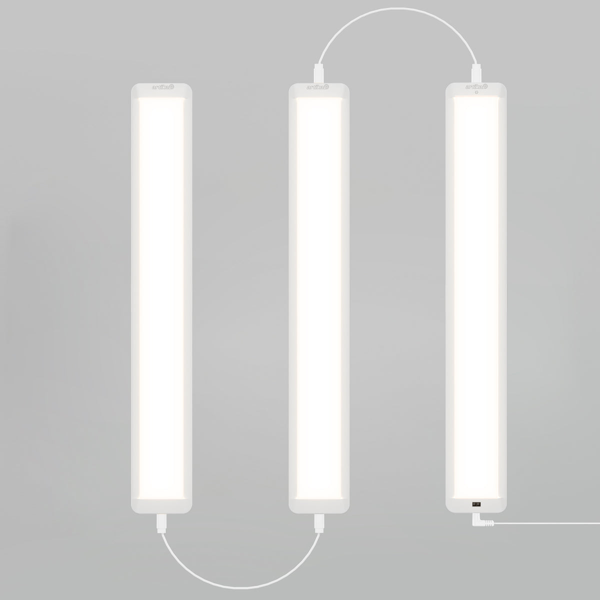 Three Artika Maestro under cabinet LED light 3CCT bars are mounted vertically in a zigzag pattern with white cables against a plain light gray background.