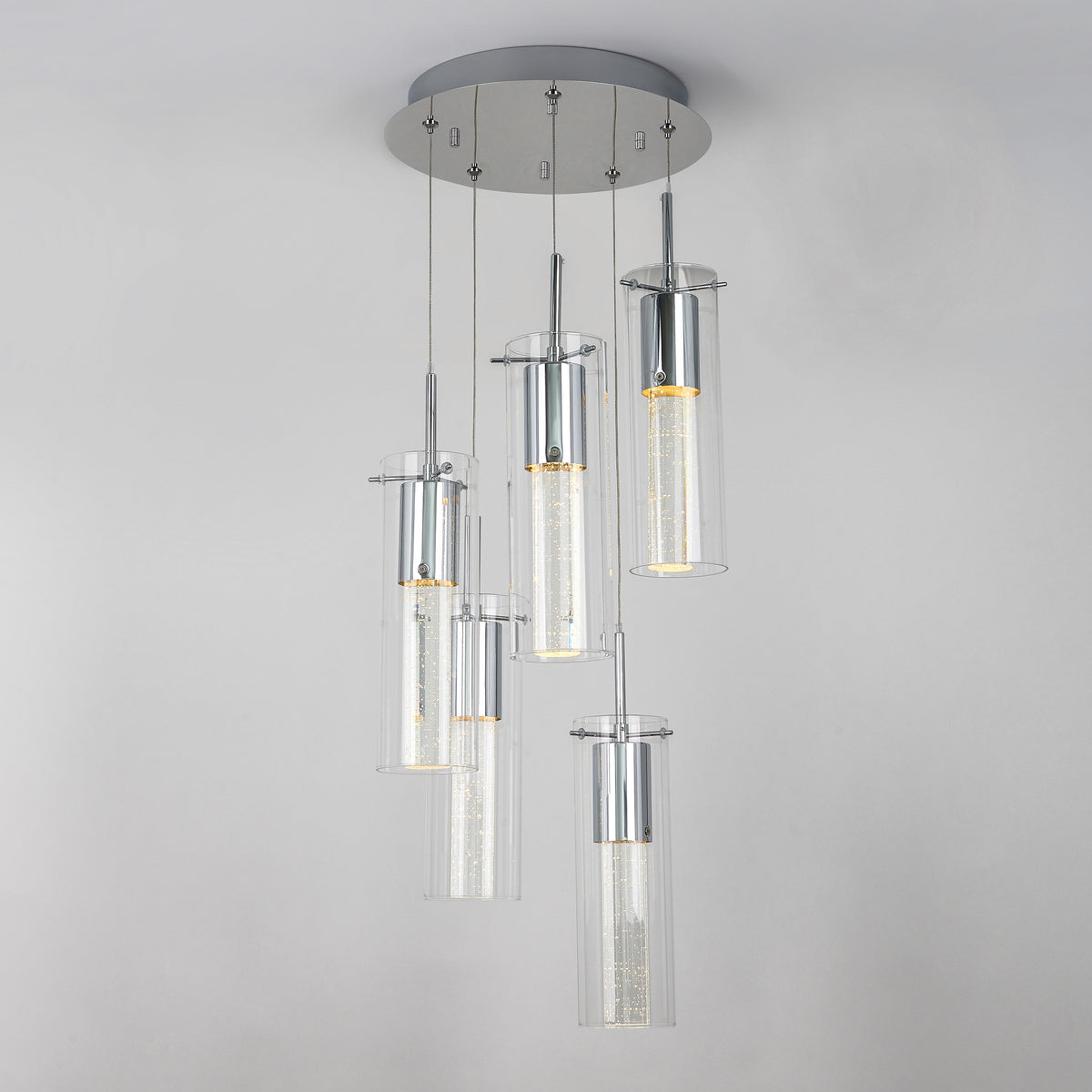 The Artika Essence 5-light LED pendant features five cylindrical glass fixtures at varying heights on a round chrome-accented base, showcasing visible LED filaments for a modern look.