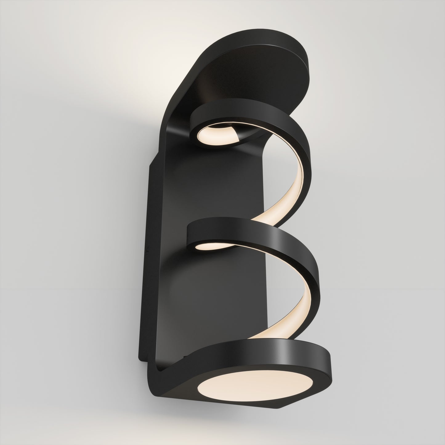 The Artika Swirl indoor-outdoor LED wall light features two spiral, glowing strips on a modern black rectangular base, casting a soft white glow on your wall.