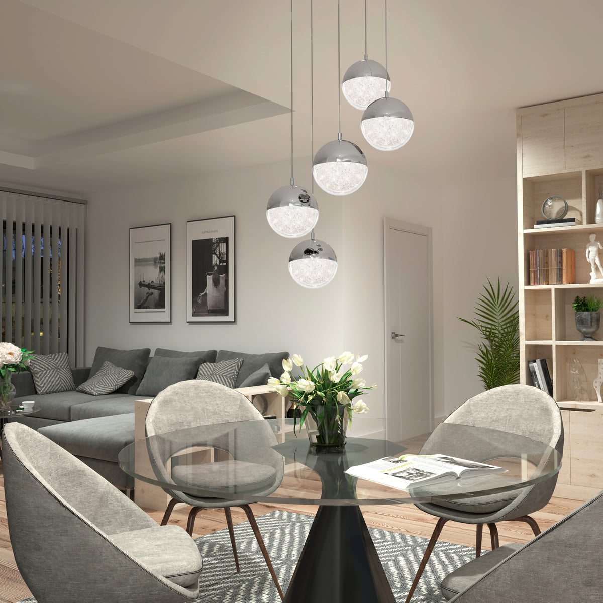A modern dining and living area with a round glass table, four gray chairs, a gray sectional sofa, wall art, Artika’s Sparkle 5-light LED pendant, indoor plants, and wooden shelves with decor.