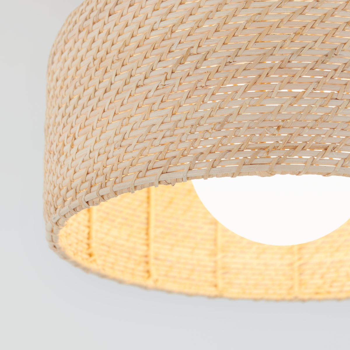 Close-up of the Emiko modern LED flush mount light by Artika, highlighting its woven rattan-style shade with a lit bulb inside and intricate texture as light filters through the natural fibers.
