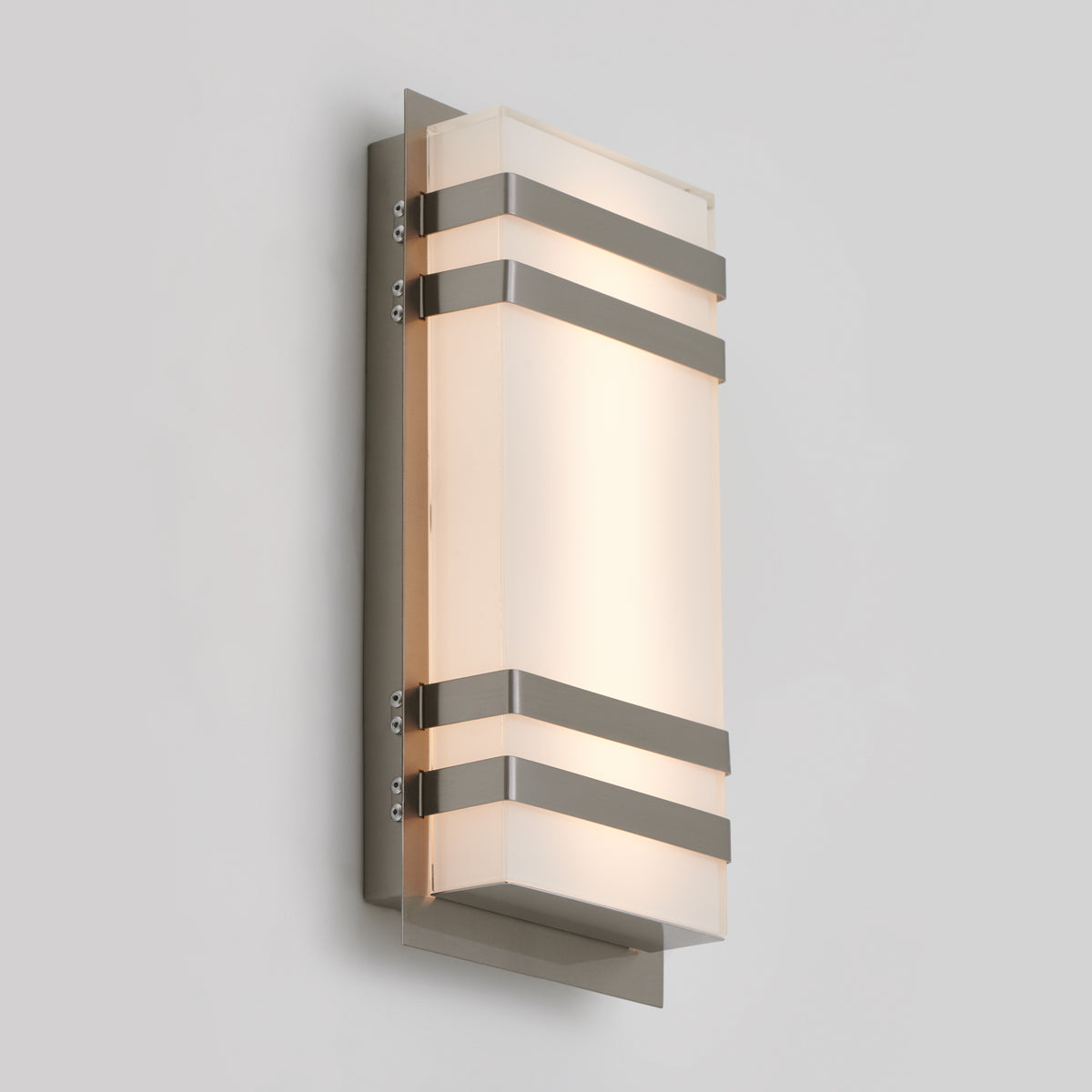 The Artika Glowbox 3 indoor-outdoor LED wall light, featuring a rectangular frosted glass shade and metal accents, is mounted on a light grey wall and emits a soft, warm glow.
