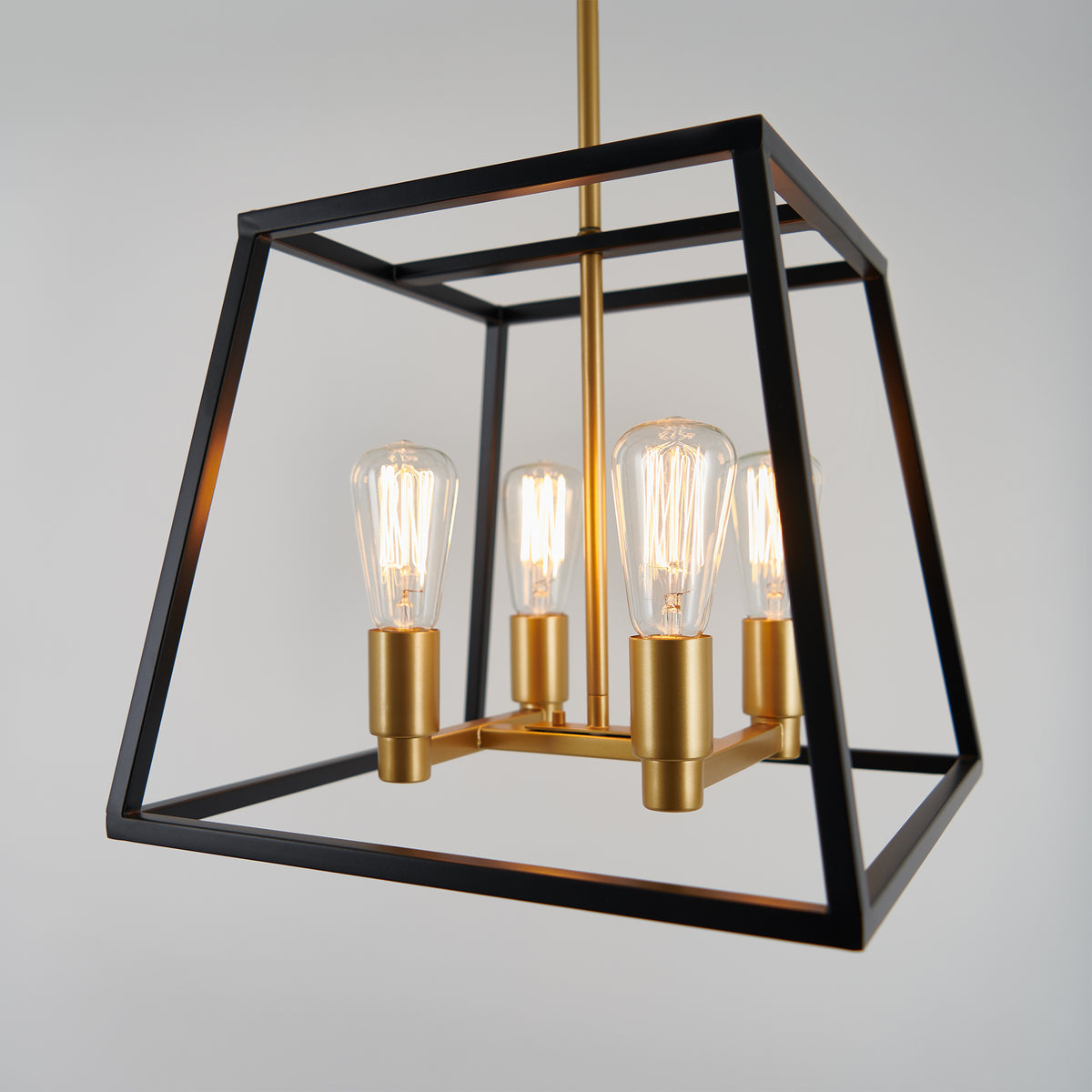 The Artika Carter Square 4-light LED chandelier features a geometric black metal frame, gold sockets, and exposed bulbs, creating modern industrial style as it hangs against a light gray background.