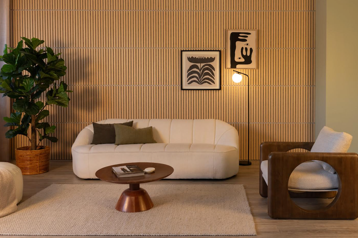 Modern living room with a white sofa, a wooden armchair, a round coffee table, a floor lamp, a large potted plant, two abstract art pieces on a wooden slat wall, and a beige rug on a wooden floor.