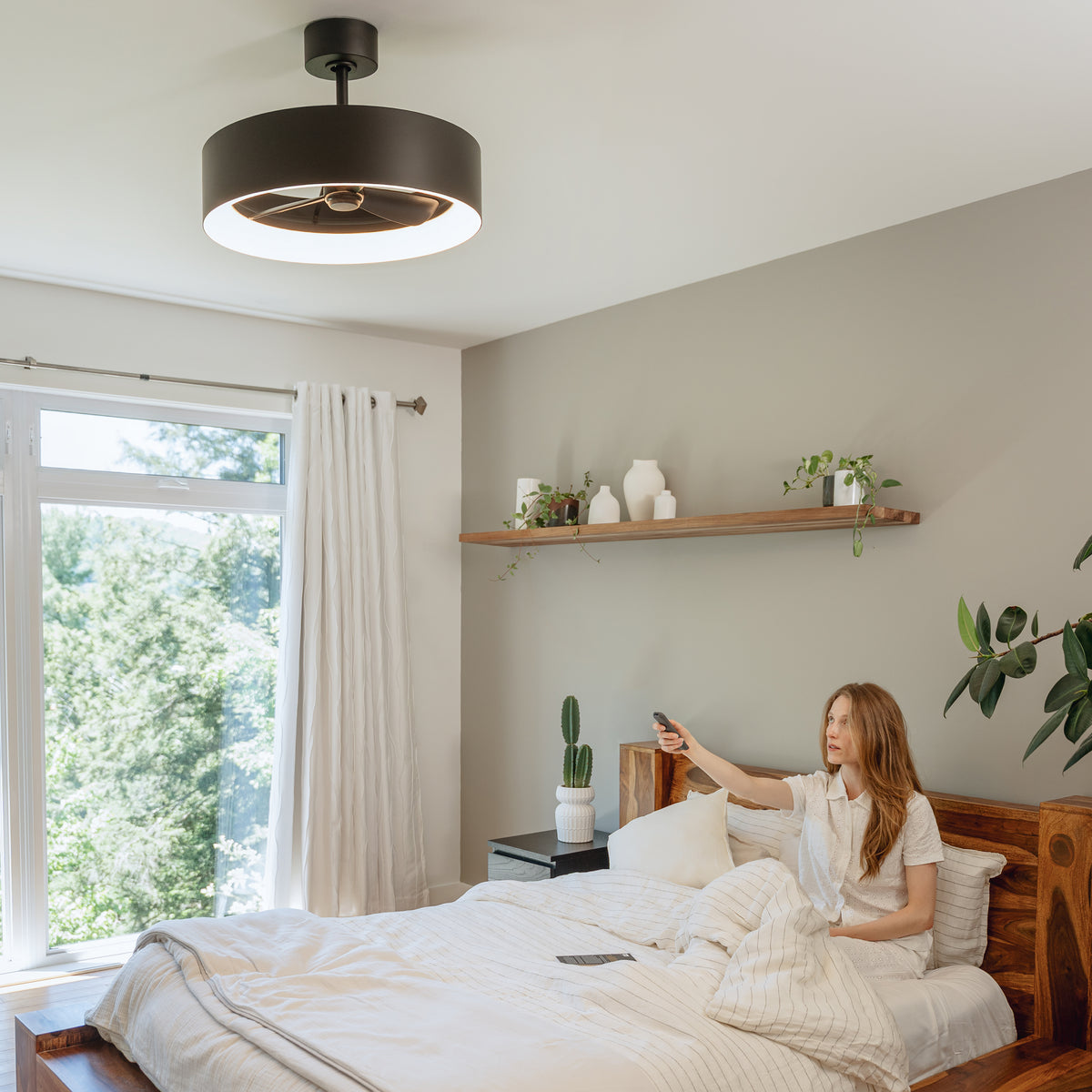 Woman in bed uses a remote to control the Artika Austin 23 in. LED fandelier ceiling fan with light and reversible airflow.