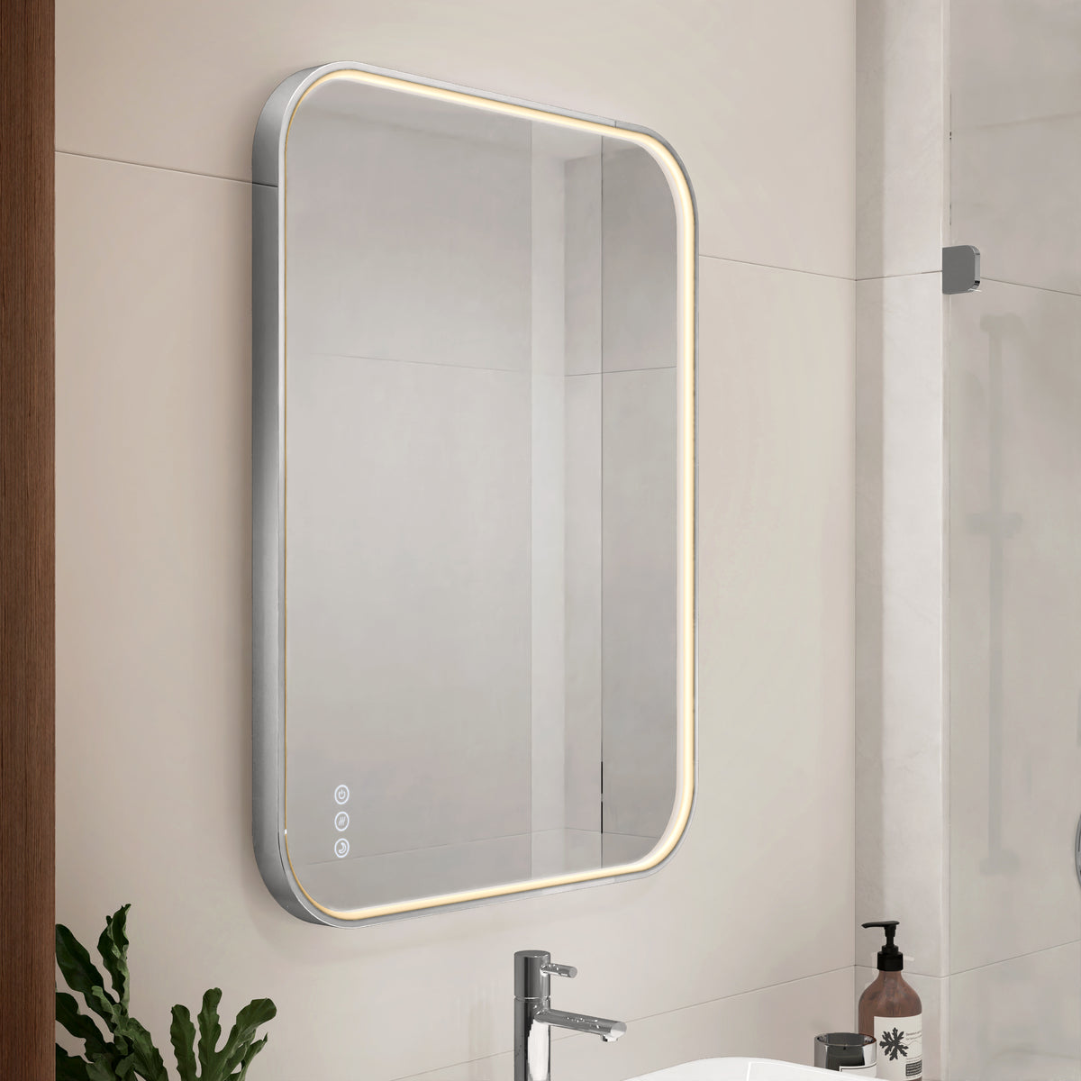 The Artika Royce Dimmable LED Mirror, featuring 3 CCT and both horizontal and vertical mount options, has a modern rectangular design with rounded corners and built-in defogger, shown above a sink with soap dispenser and plant nearby.