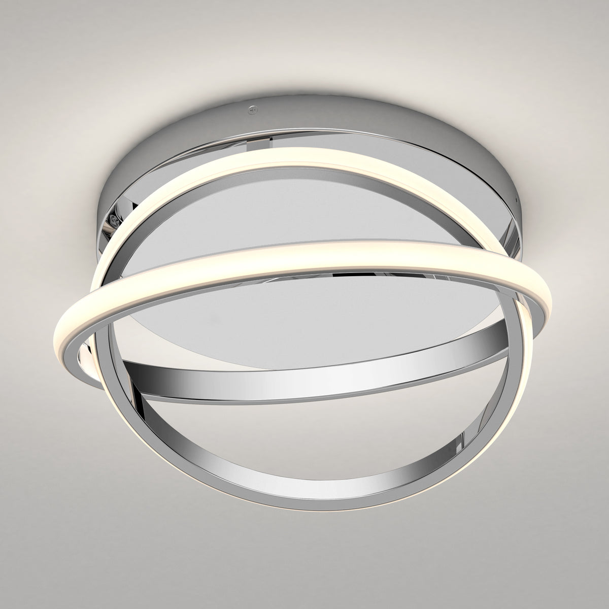 The Artika Orbia modern LED flush mount light 3 CCT features a circular chrome base with two intertwined rings—one illuminated, one reflective—creating a striking centerpiece when mounted on a white ceiling.