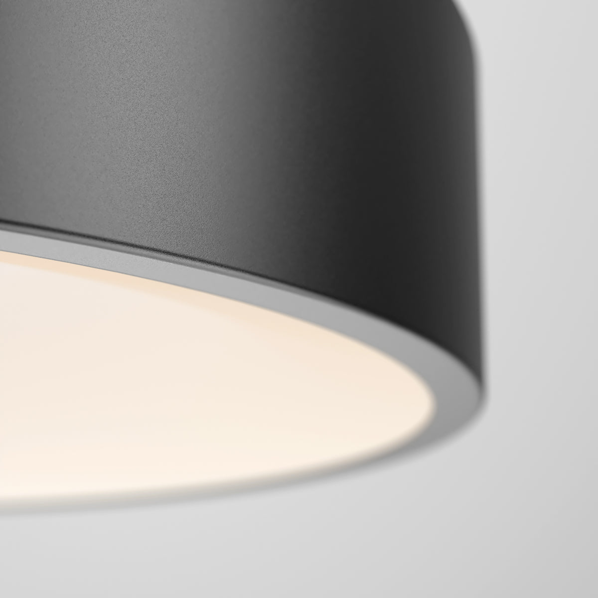 Close-up of the Aiden LED pendant light by Artika, a modern round dark gray fixture with a smooth surface, casting a soft warm glow against a light gray background.