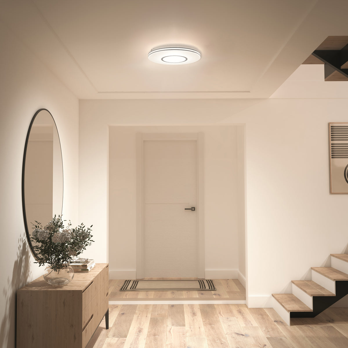 A modern hallway with wood floors, a round mirror, console table, plant, and Artika Horizon 13 in. LED flush mount ceiling light.