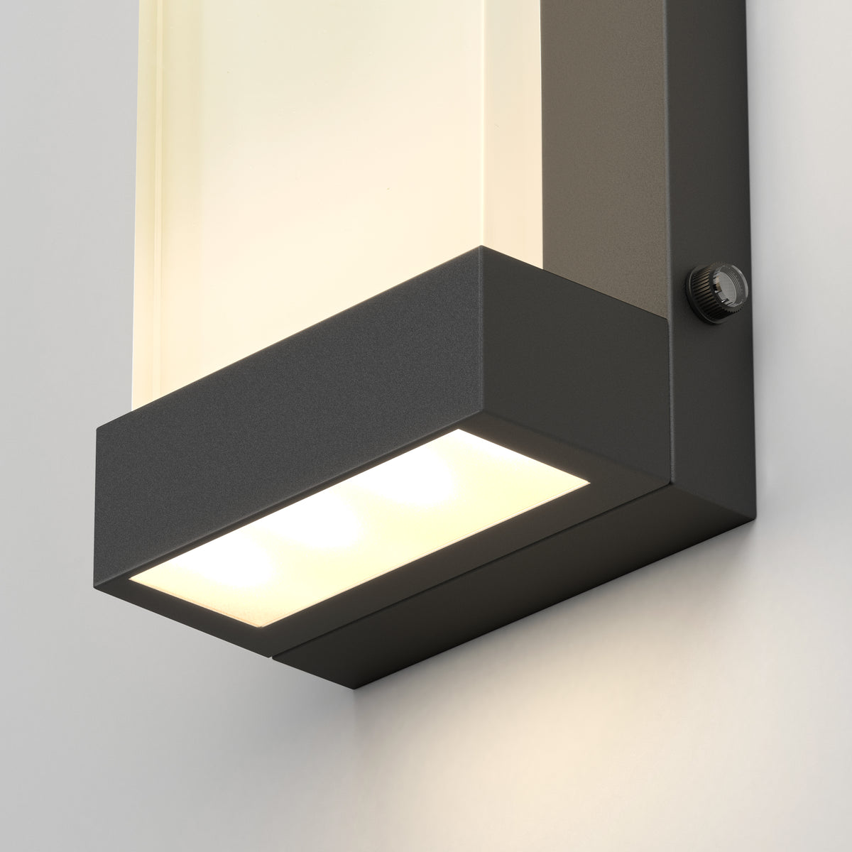 Close-up of the Artika Glacier indoor-outdoor LED wall light, featuring a rectangular black metal frame and frosted glass, casting a bright white glow on a light-colored wall.