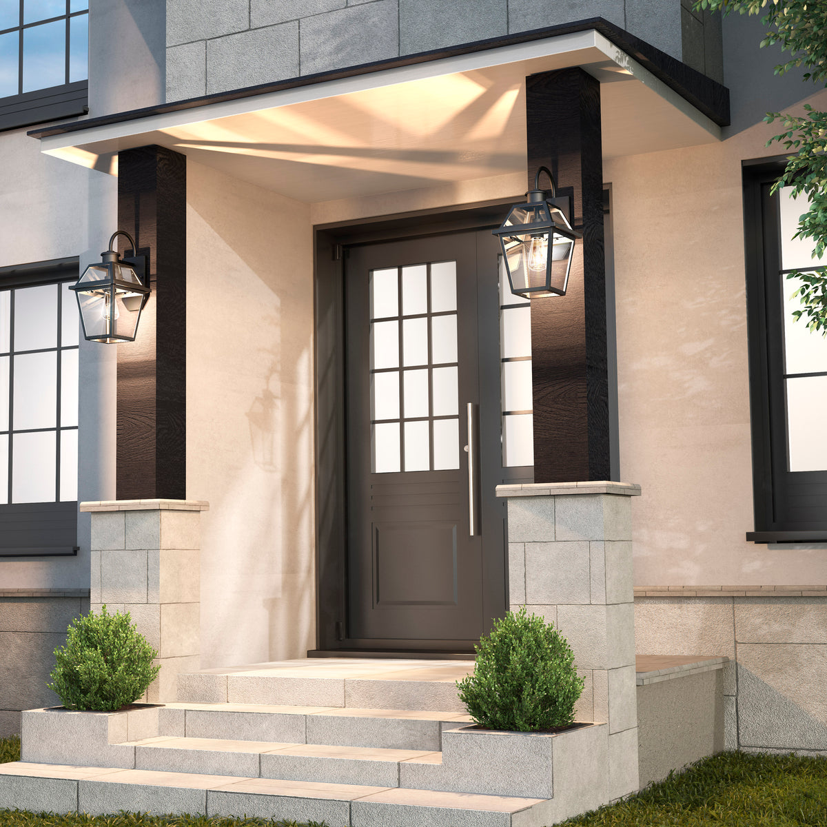 Modern front entrance with a black door featuring glass panes, two Artika Colonial outdoor lantern wall lights on either side, stone steps, and small green shrubs flanking the entryway.