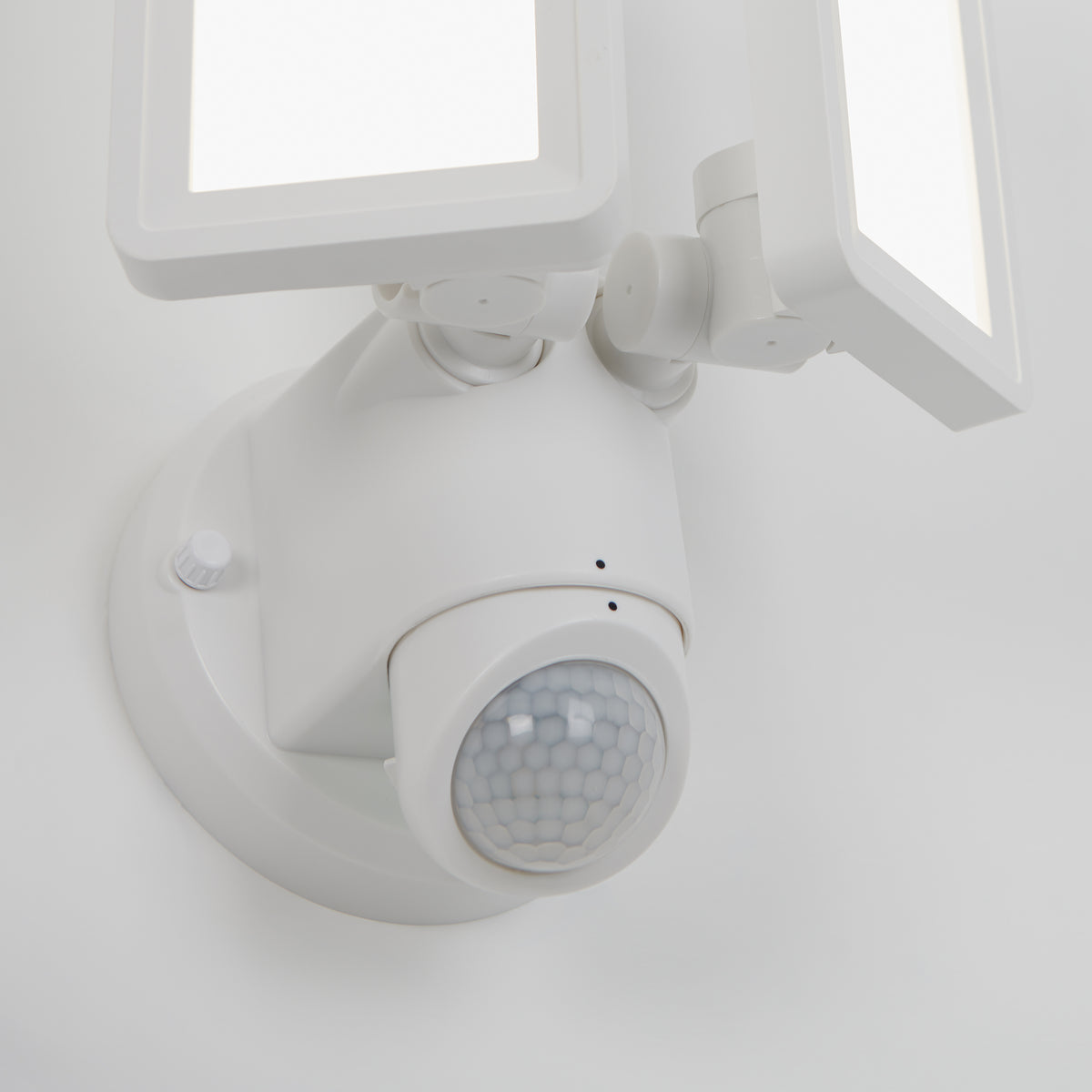 A close-up of the Artika Sentinel outdoor Flat Panel Security light, featuring two rectangular LED panels and a round motion sensor, mounted on a white wall.