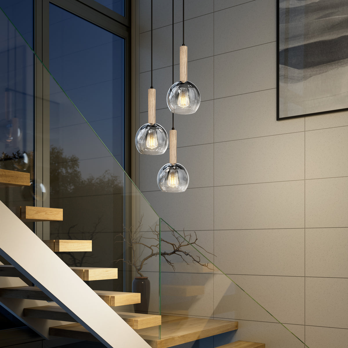 Three Ardel Spiral 3-Light Pendants by Artika with wooden tops and glass globes hang near a wooden staircase with glass railing in a modern interior, featuring a large window and abstract wall art in the background.
