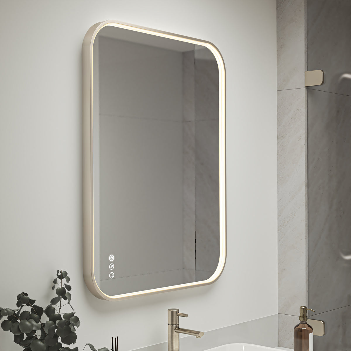 The Artika Royce Dimmable LED Mirror (3 CCT) is a rectangular, wall-mounted mirror with rounded edges and built-in adjustable brightness and defogger, shown above a sink with a gold faucet, soap dispenser, and small plant nearby.