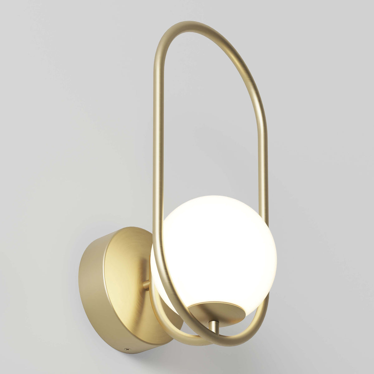 The Artika Bloom LED Sconce 3 CCT features a matte gold oval metal frame and round white frosted glass shade, emitting soft light when mounted on a light grey wall.