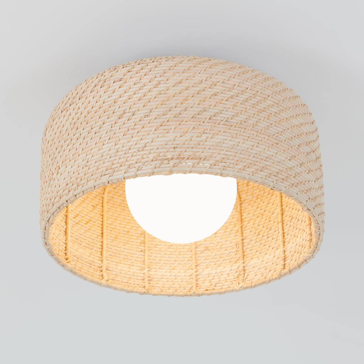 The Artika Emiko modern LED flush mount light 5 CCT features a woven beige rattan shade and a glowing white bulb in the center, all set against a light gray background.