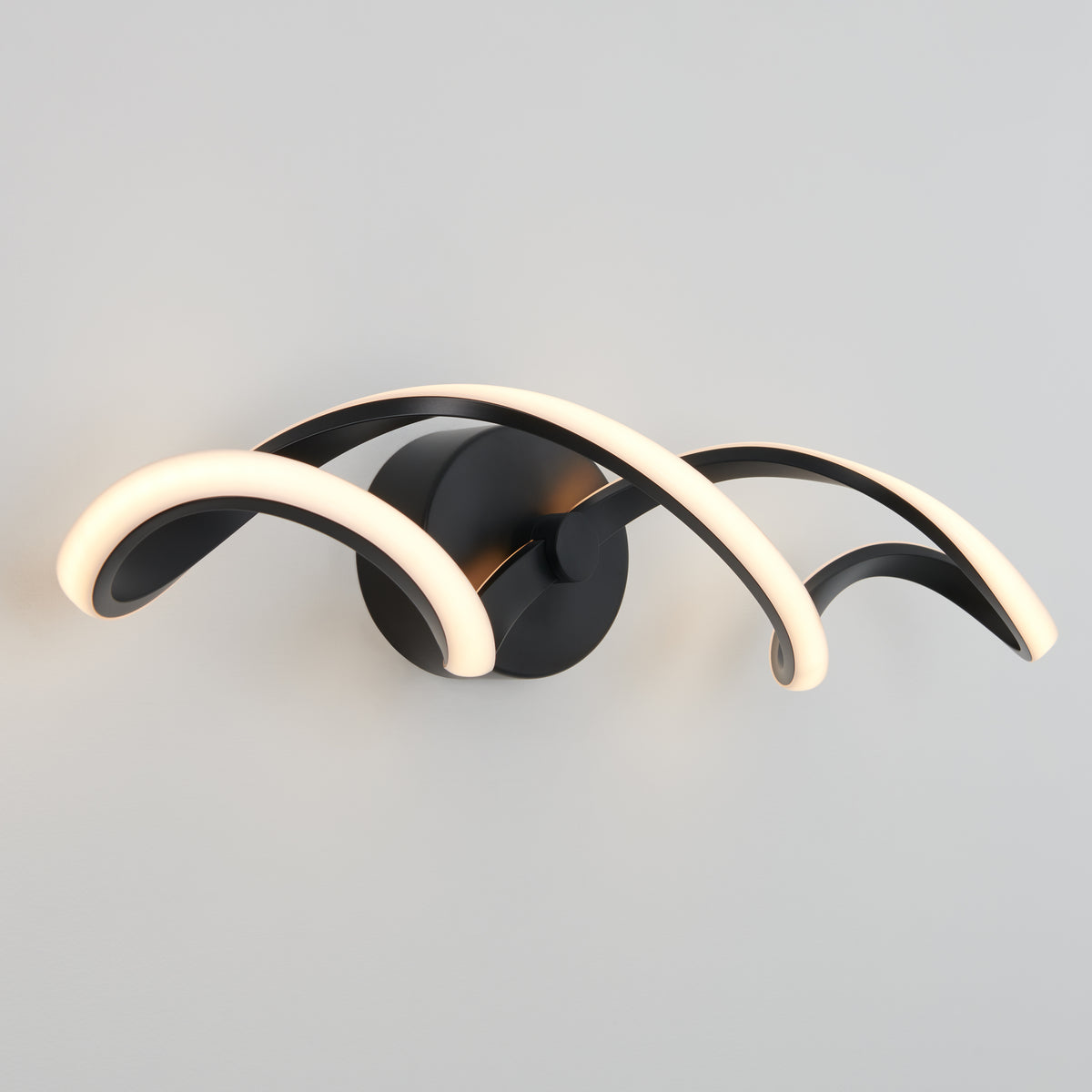 The Artika Swirl LED bathroom vanity light features three curved black arms with integrated LEDs, mounted on a round black base for a soft white glow against a light gray wall.