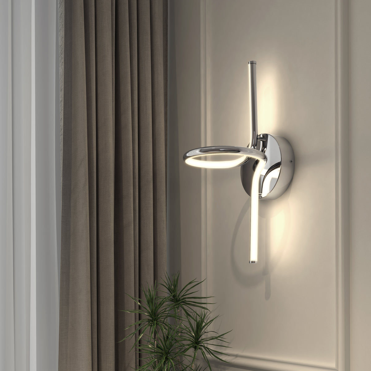 Artika’s Swirl LED Sconce, a modern circular chrome wall light with adjustable brightness, is mounted on a light gray wall next to taupe curtains, illuminating a green leafy plant below.