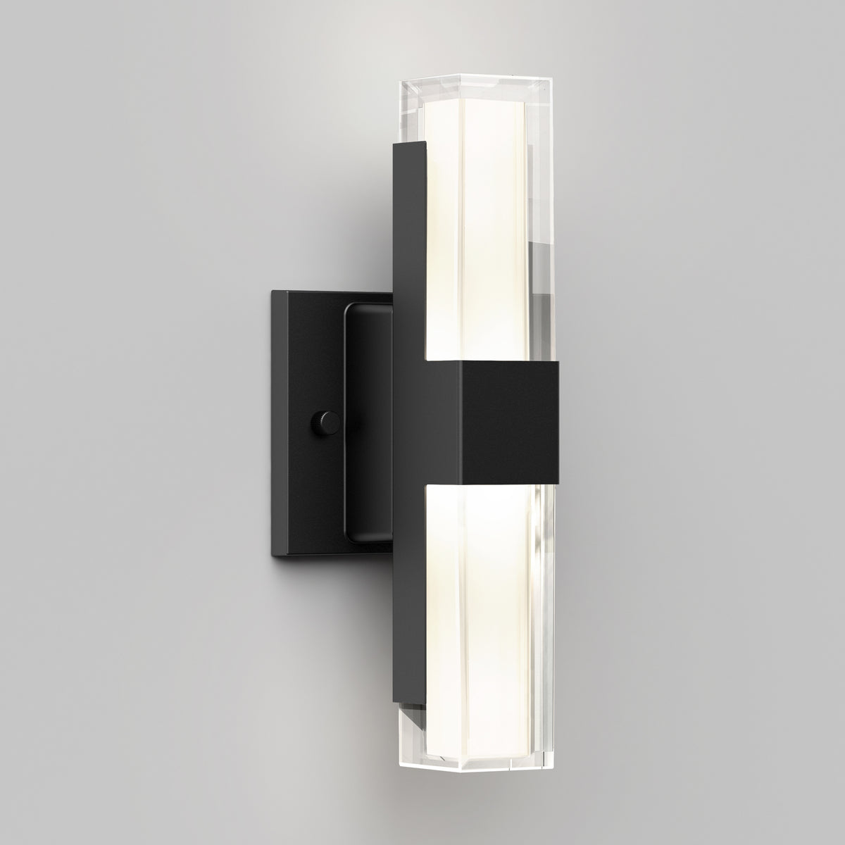 The Artika Gemini indoor-outdoor LED wall light features a rectangular black metal base and a vertical frosted glass fixture, casting a soft white glow against a light gray wall.