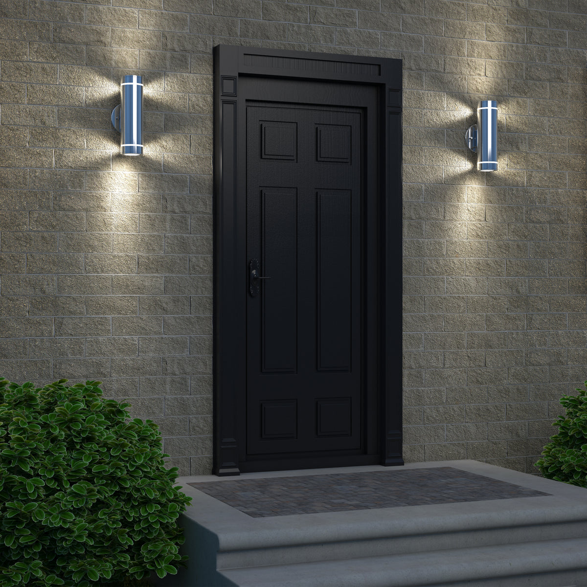 A black door set in a brick wall is illuminated by two Artika C7 indoor-outdoor wall lights on either side, while two green bushes frame the steps leading up to the entrance.