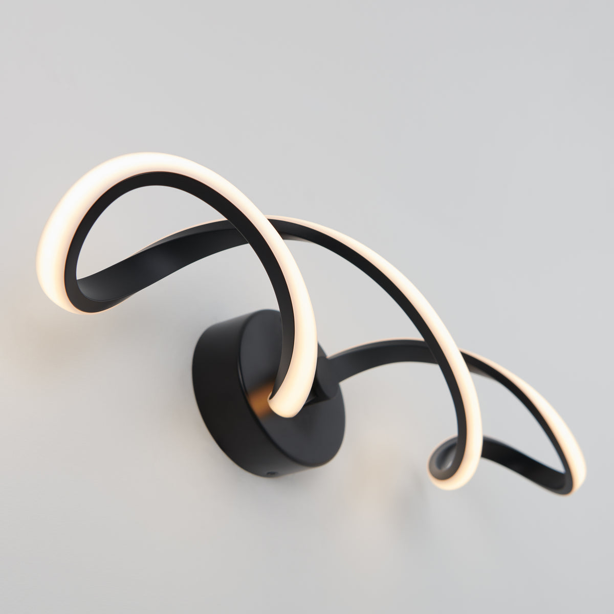 The Artika Swirl LED bathroom vanity light features two curved black metal arms with integrated LED strips, forming a modern, abstract design that enhances any light-colored wall.