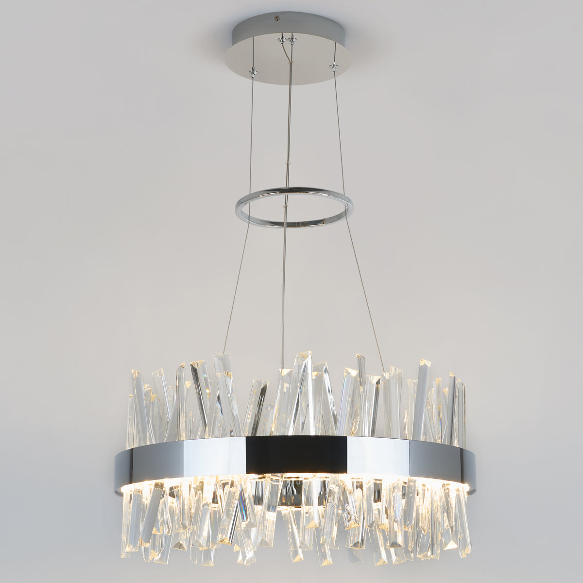 The Artika Enchanted LED pendant light features a circular chrome frame suspended by cables, with irregular clear glass prisms that emit soft white light, creating a modern look against any white ceiling.