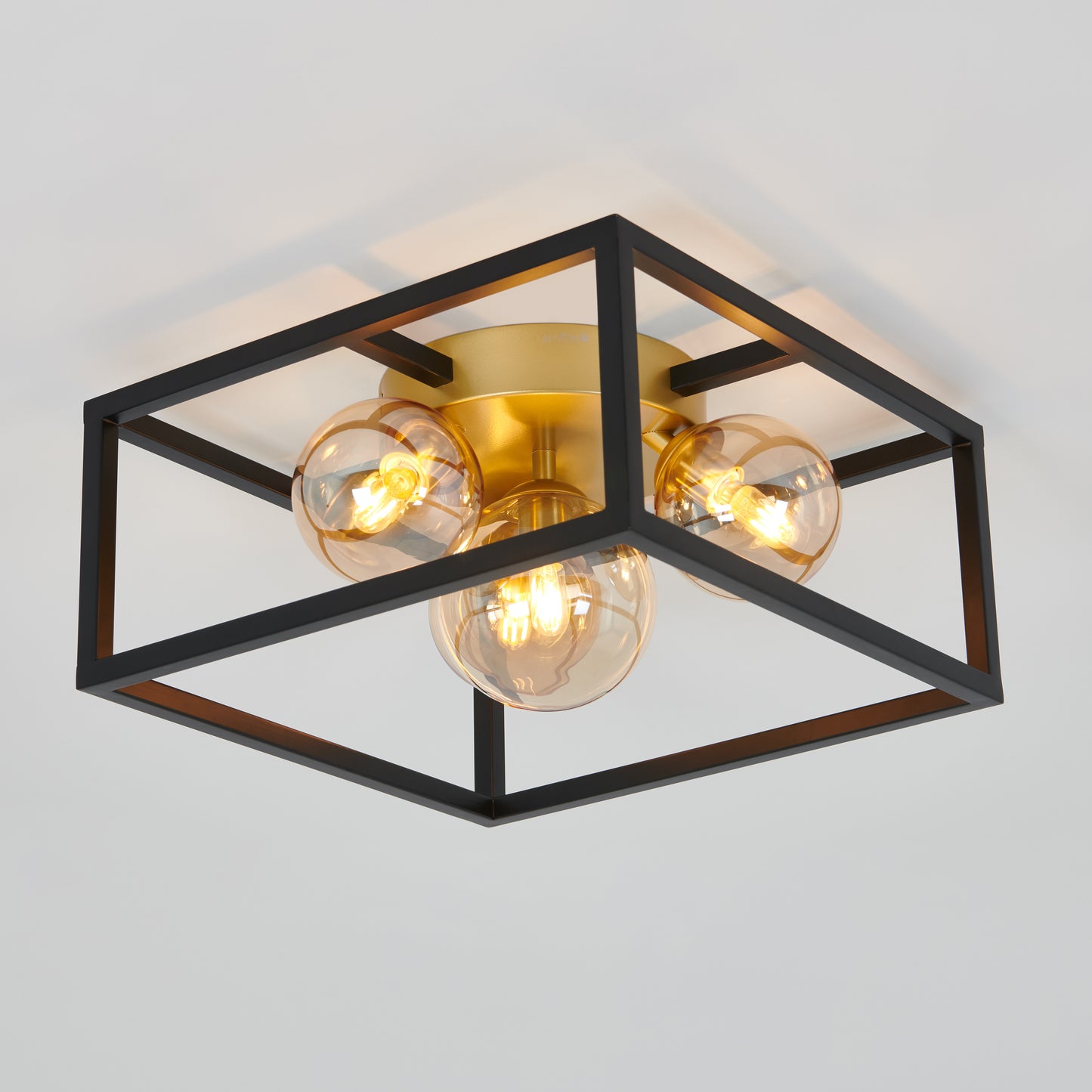 The Artika Griffintown flush mount is a modern ceiling light with exposed bulbs, a black open square metal frame, and a brass base, installed on a white ceiling.