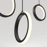 Close-up of modern, circular pendant lights with black frames and glowing white edges, suspended against a plain, light background. The focus is on the illuminated rings, creating a minimal and contemporary look.