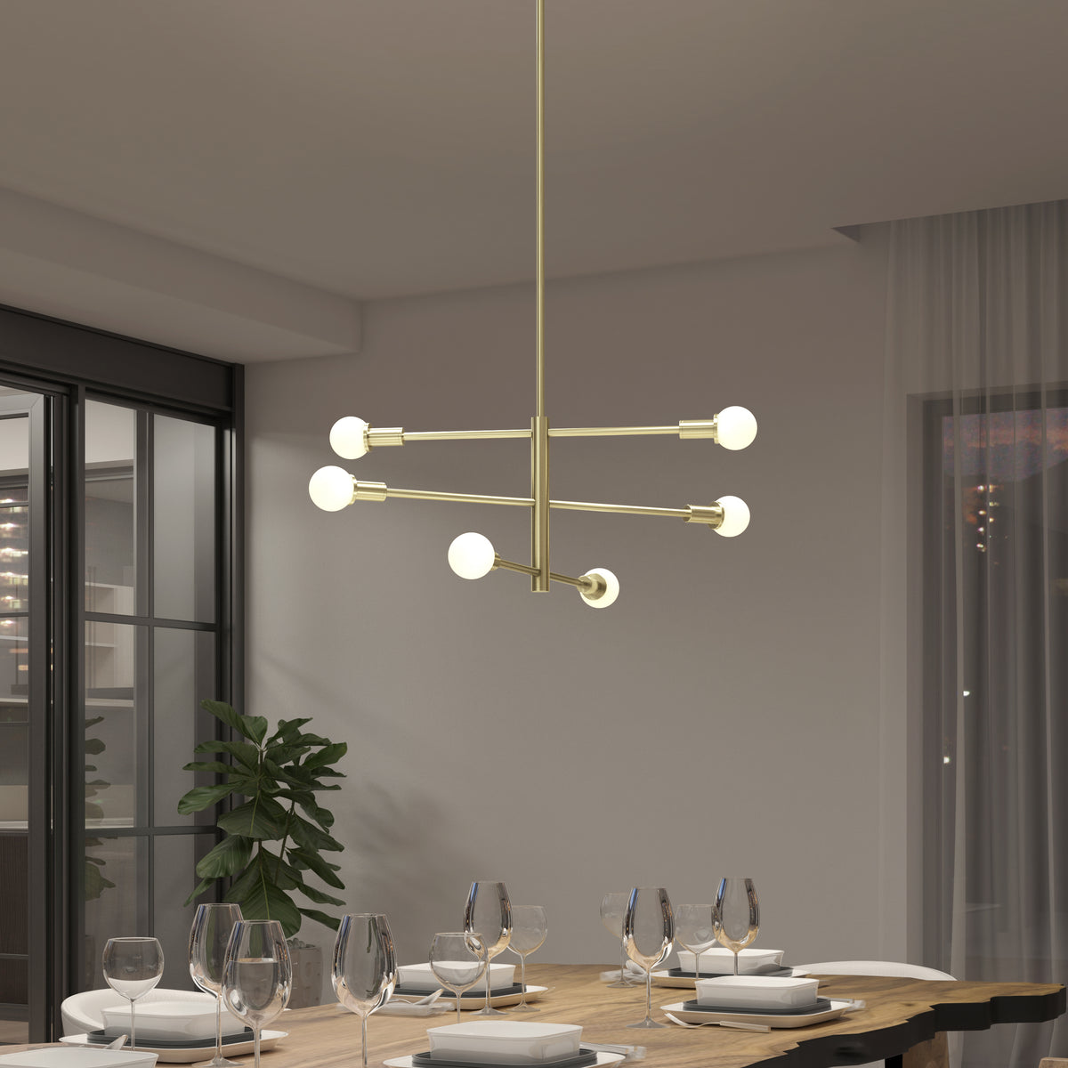 A modern dining room with a gold chandelier featuring six round bulbs, a wooden table set with plates and glasses, a potted plant, and large windows with sheer curtains in the background.