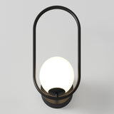 A modern wall sconce featuring a glowing white globe light enclosed within a black oval metal frame, mounted on a circular base against a light gray background.