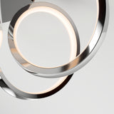 Close-up of a modern, circular LED light fixture with metallic rings and soft white illumination against a plain light gray background.
