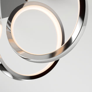 Close-up of two overlapping Swirl Ribbon LED flush mount lights by Artika, featuring sleek metallic silver frames. The dimmable fixtures emit a soft, warm glow against a plain light gray background, highlighting their modern minimalist design.