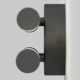 A modern black wall-mounted light fixture with two round, disc-shaped lights extending outward, attached to a rectangular base against a plain light gray background.