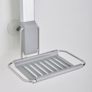 A close-up of the Artika Ulysse hanging Shower Caddy, featuring a silver metal frame and grey slatted base, mounted on a white wall using a suction cup.