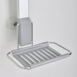A close-up of a wall-mounted, silver metal soap dish with slotted drainage and a suction cup attachment on a white background.