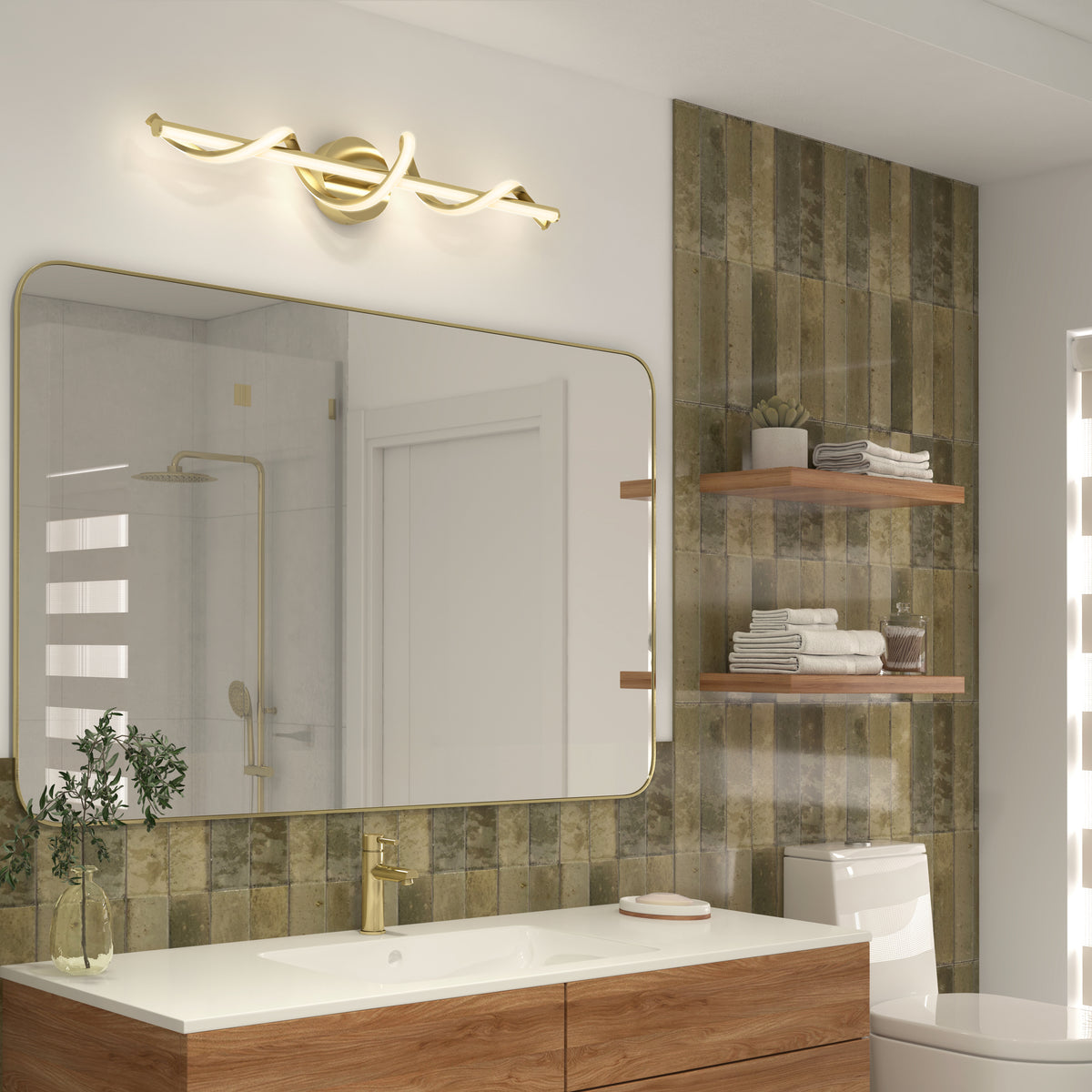 Modern bathroom with a wood vanity, gold faucet, and large rectangular mirror. Wall features greenish tiles, floating shelves with towels and decor, and a sculptural gold light fixture above the mirror.