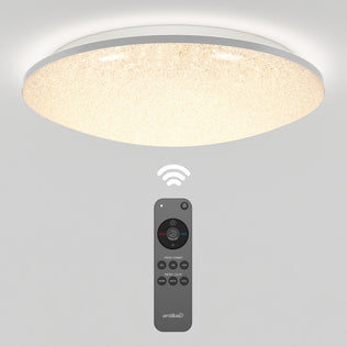 The Artika Sparkle LED flush mount light is ceiling-mounted and illuminated, with its multi-button remote control (for wireless operation) shown below. Both are set against a plain white background.