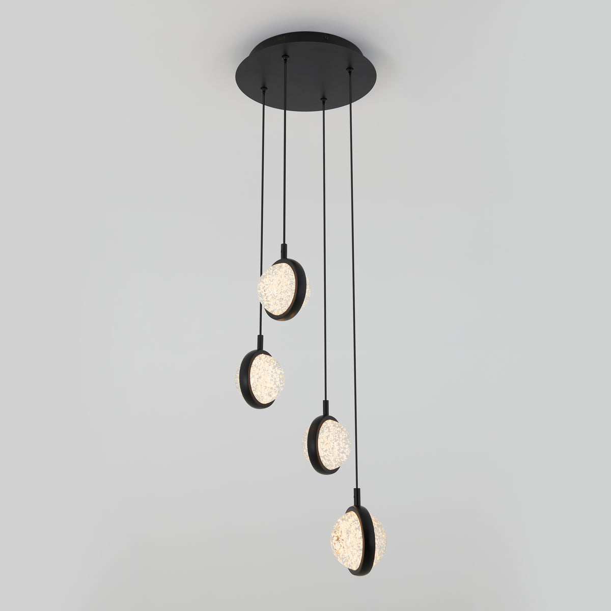 A modern ceiling light fixture with four hanging pendant lights, each featuring a circular design with textured, illuminated glass, suspended at different heights by black cords from a round black base.