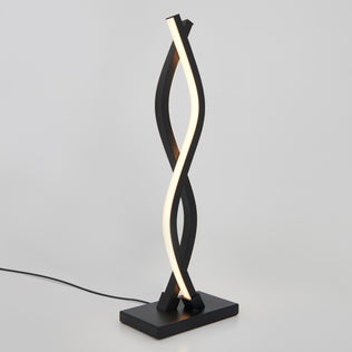 The Artika Wave LED Table Lamp showcases a modern, twisted ribbon design with a black base and frame and a spiraling white light strip. Plugged in, it’s displayed against a plain white background.