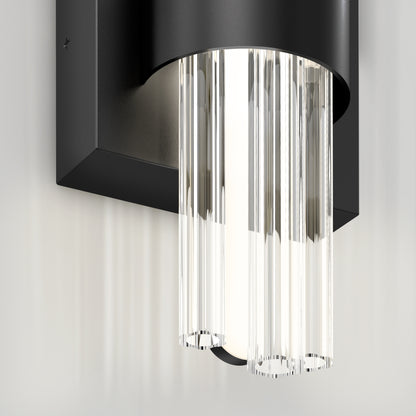 Close-up of the Artika Dorado LED contemporary wall sconce 3 CCT, featuring a black rectangular base and vertical clear glass rods for sleek, modern illumination against a light-colored wall.